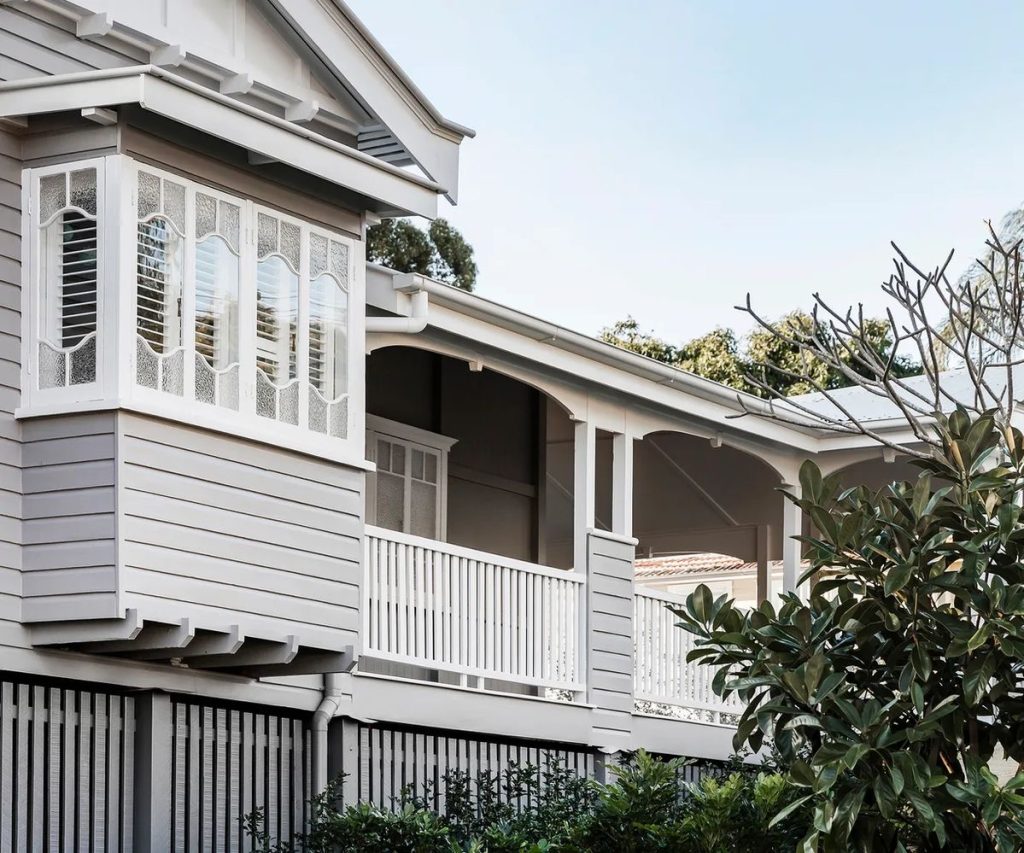 Traditional Queenslander house with grey weatherboard exterior and white verandah.