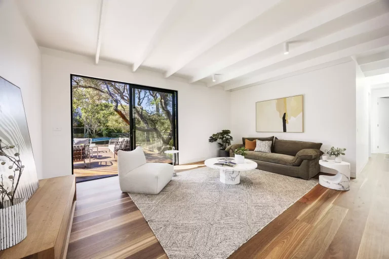 Bright, modern living room with wooden floors, white walls, stylish furniture, large sliding glass doors, and access to a sunny outdoor deck.